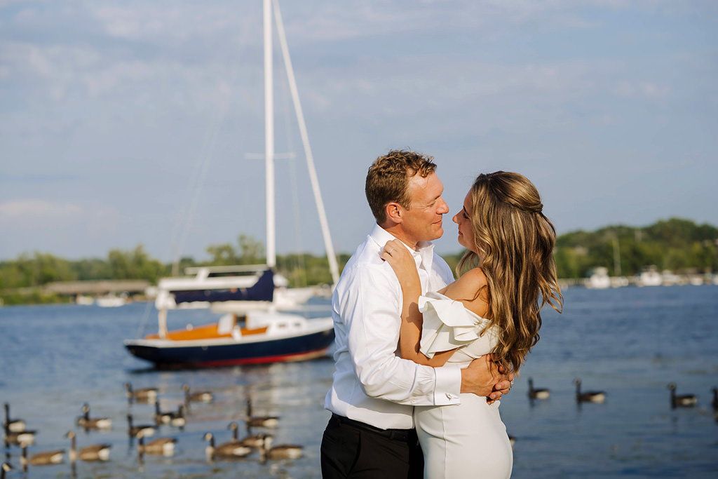 lakeside newlyweds embrace in front of geese and sail boat