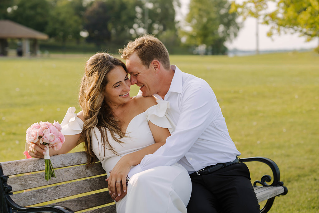 newlyweds laugh and embrace on park bench in excelsior