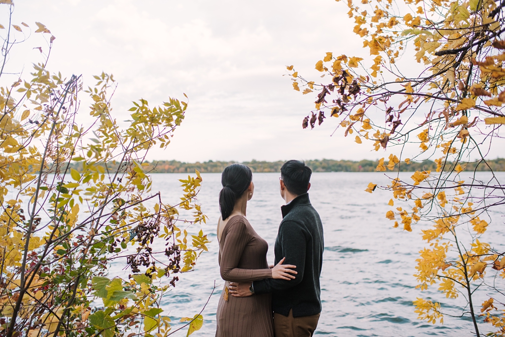 couple stand in fall foliage beside bde maka ska