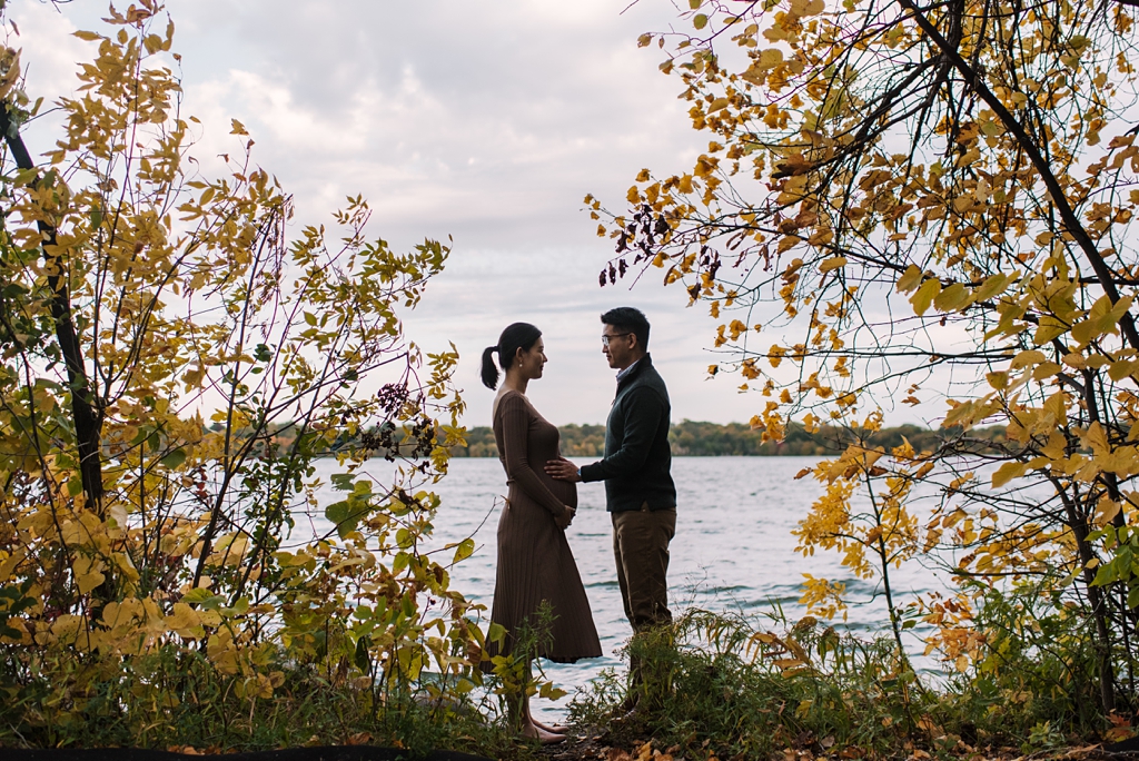 couple nearly silhouetted with fall foliage in front of lake
