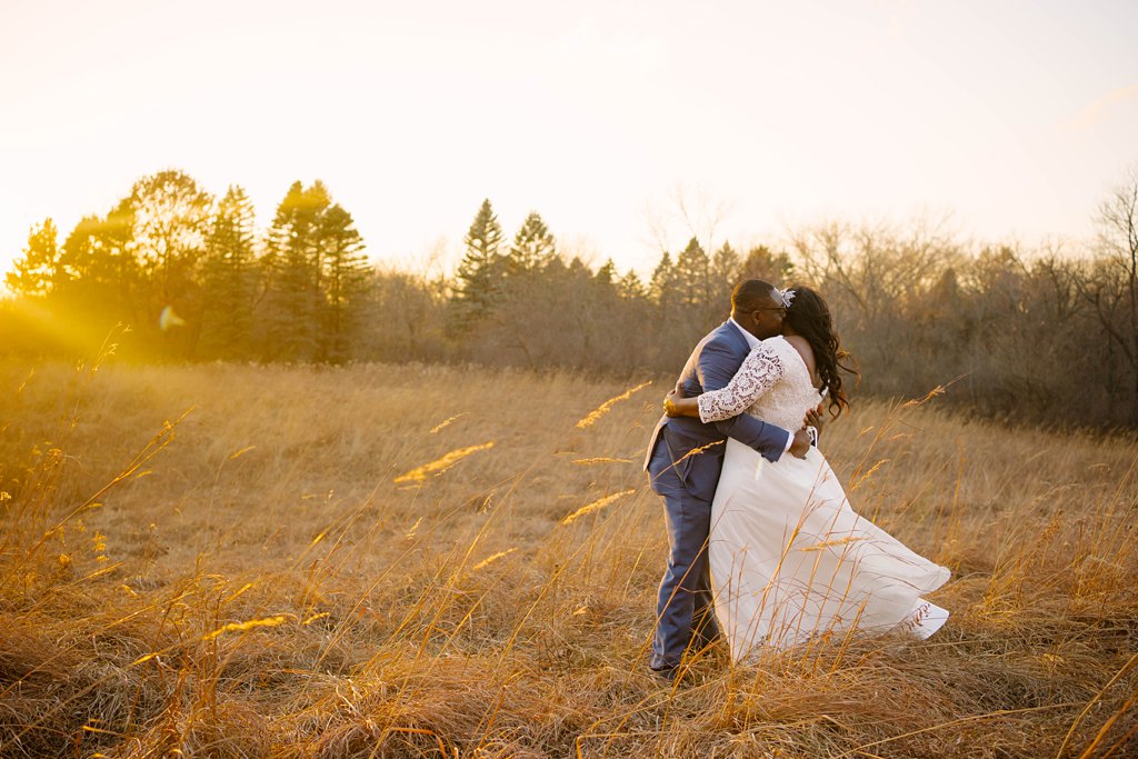 groom hugs bride in field at sunset