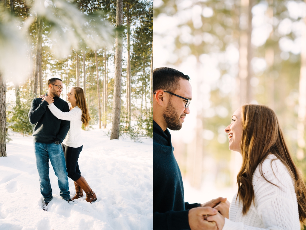 couple embracing in snow during winter engagement session beneath pines