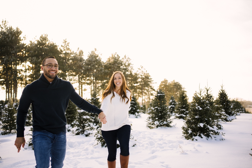 couple walking through snow at tree farm engagement session