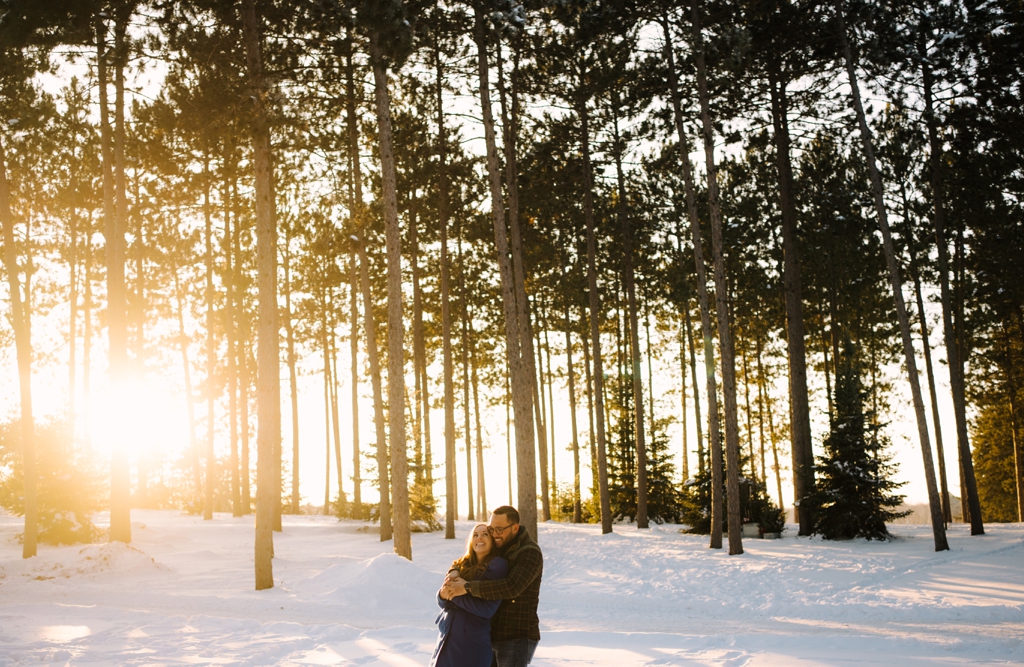 sunset winter engagement photo couple embracing beneath pine trees