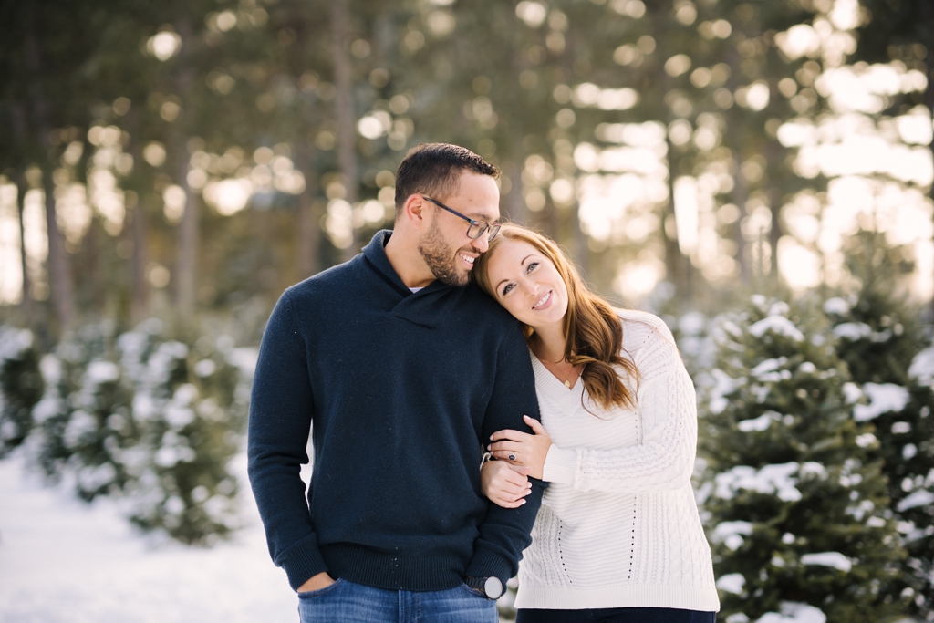 engaged couple walking together through snowy tree farm