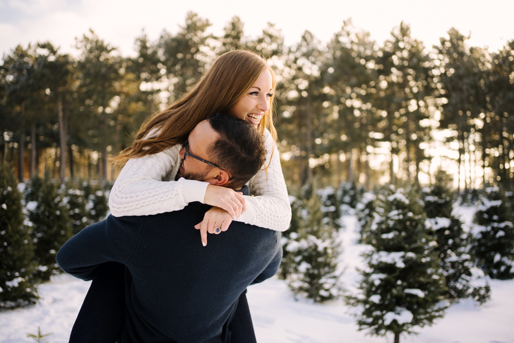 engaged couple hugging in snow with trees at sunset