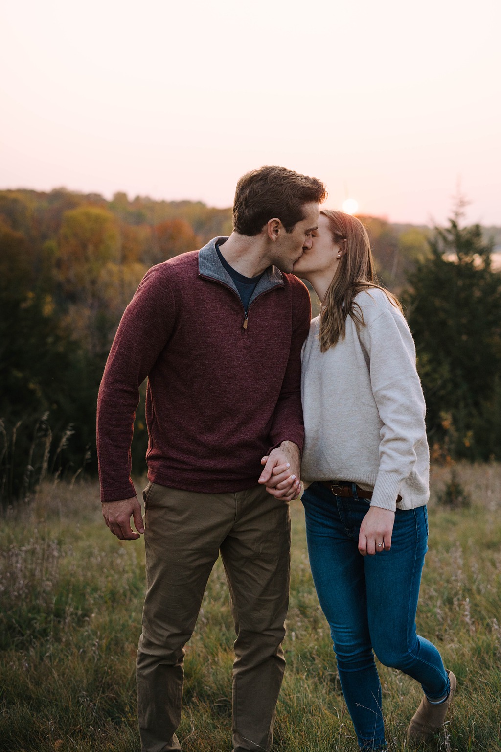 engaged couple kiss in front of fall leaves