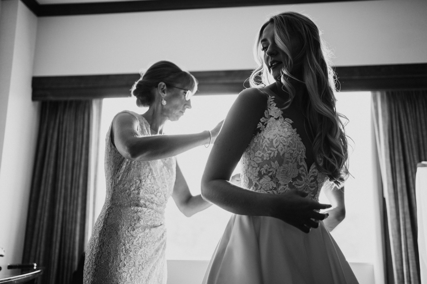 bride being fastened into dress by mother