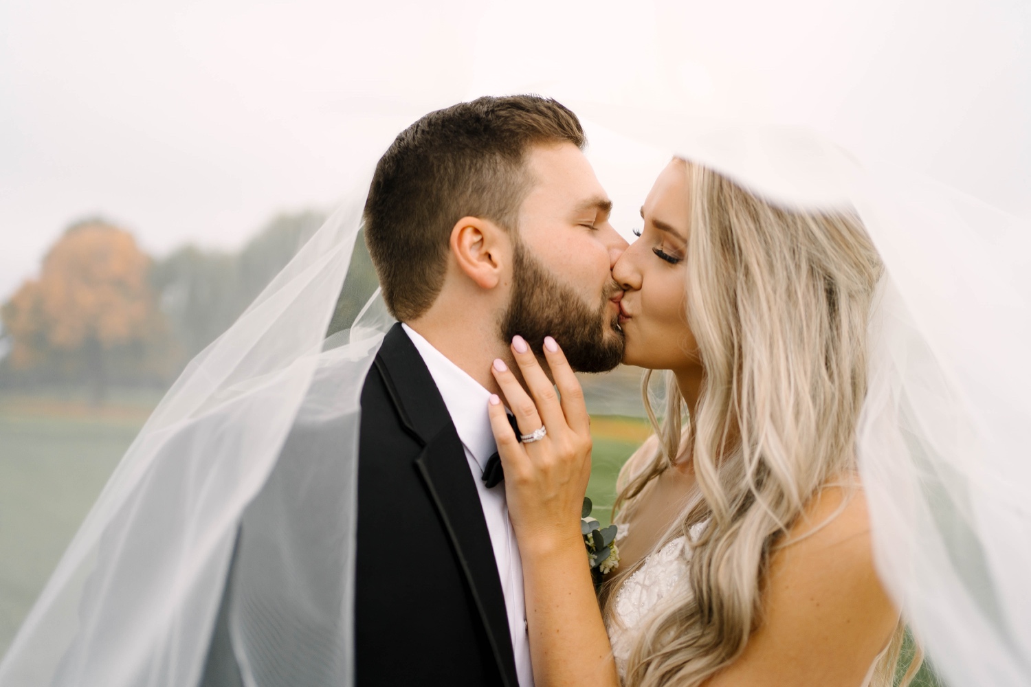 bride and groom kiss beneath veil after outdoor wedding
