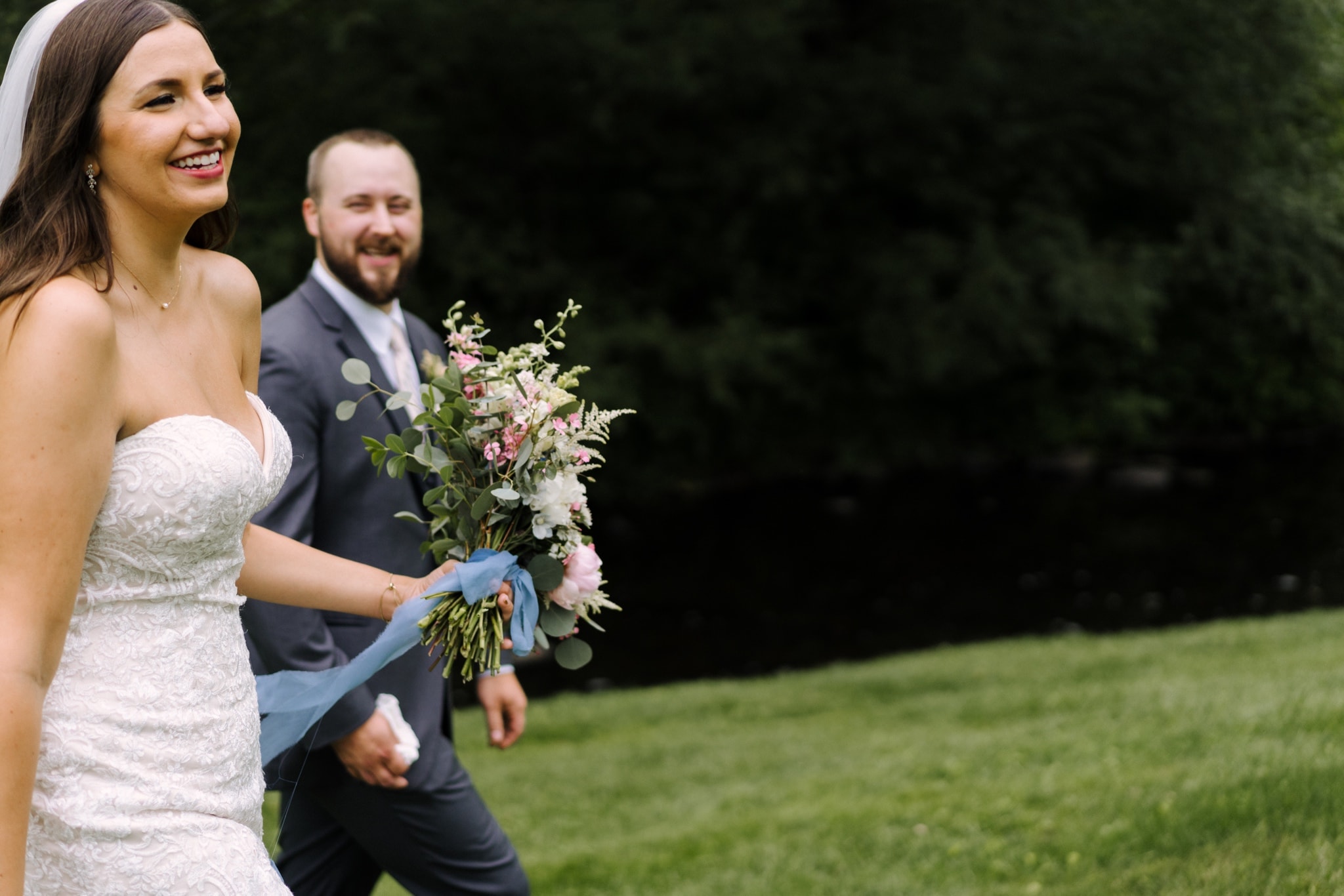 bride and groom walking through green field