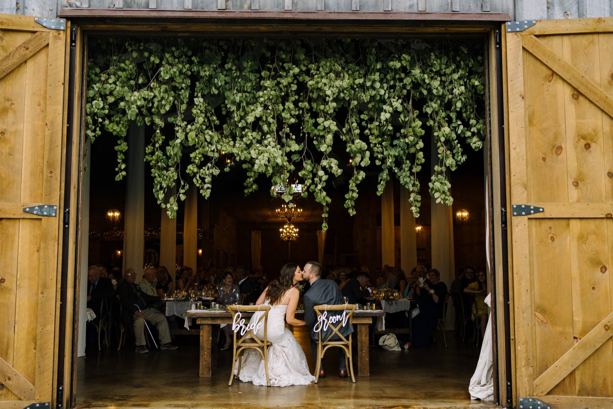 outside looking in at rustic wedding reception bride and groom kiss