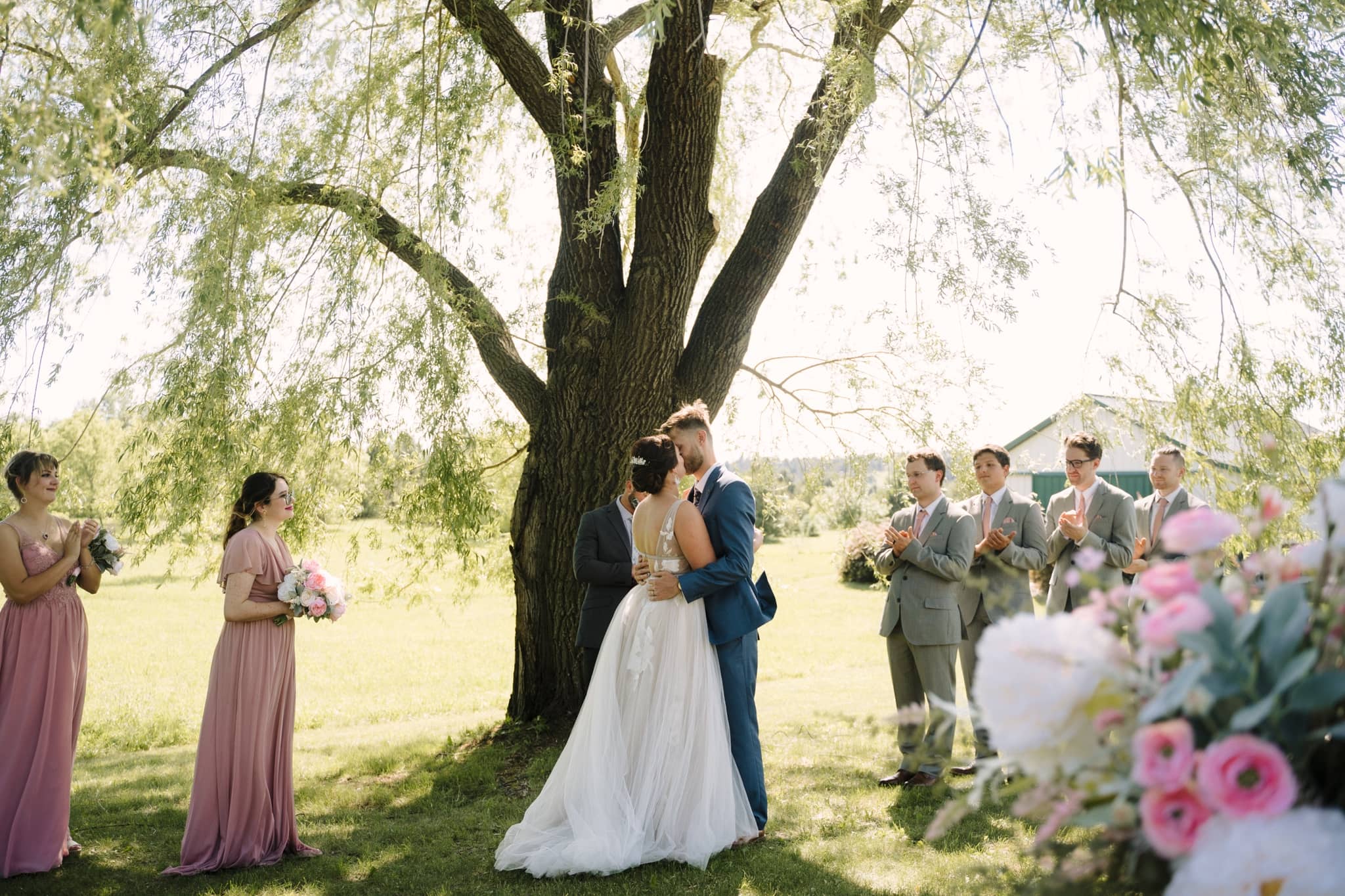 first kiss beneath willow tree at garden party wedding