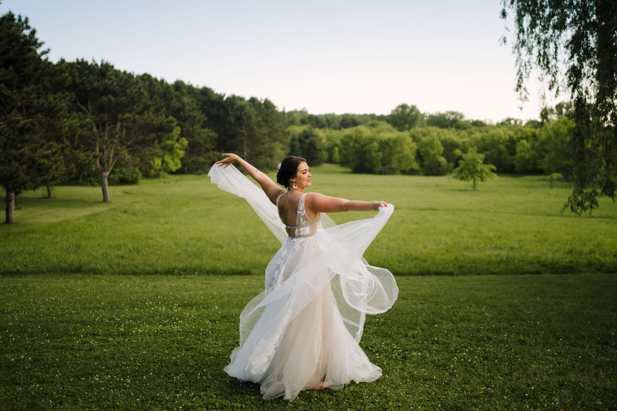 bride twirls in wedding dress in green field
