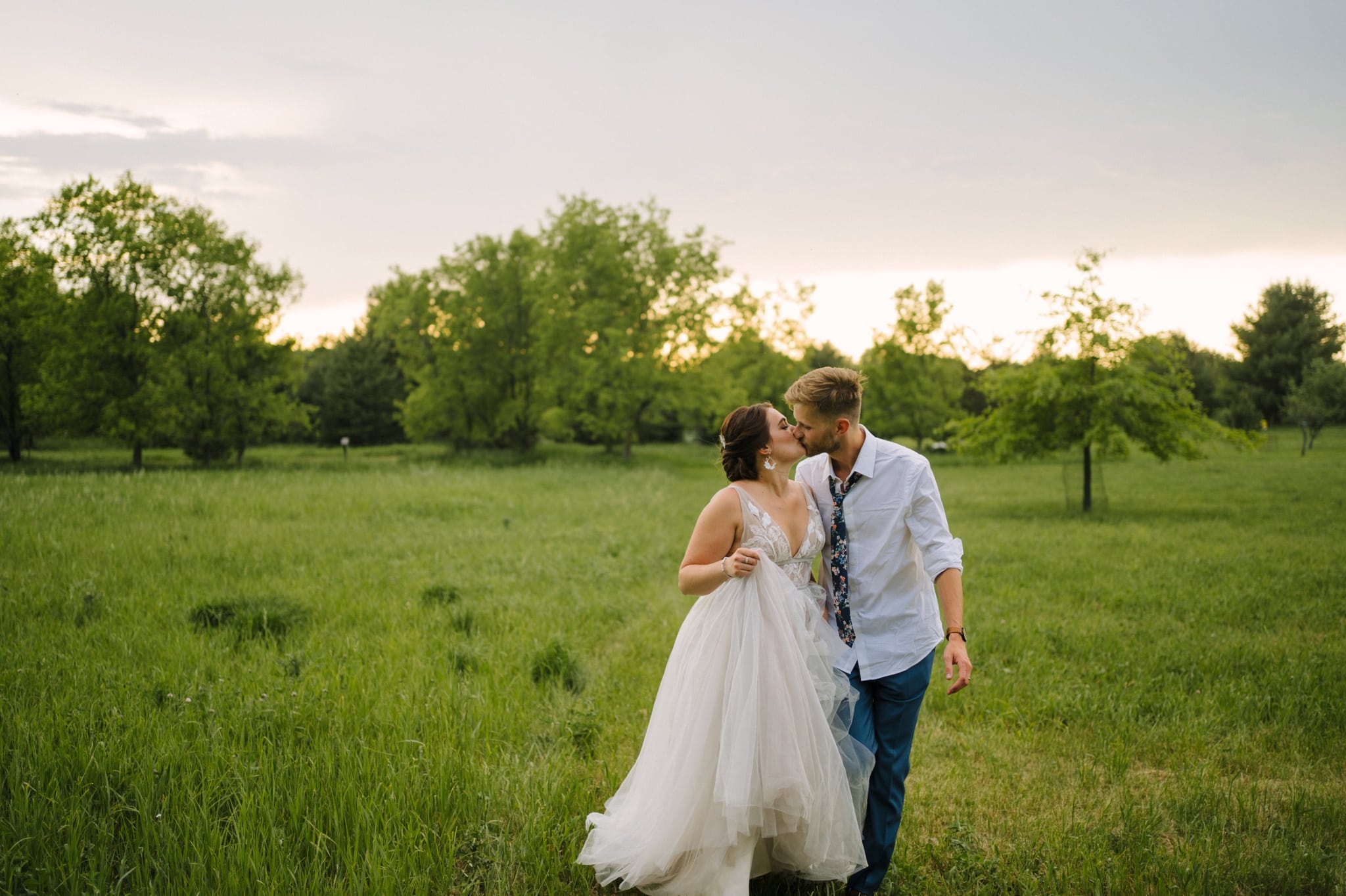 couple kiss in green field at garden party wedding